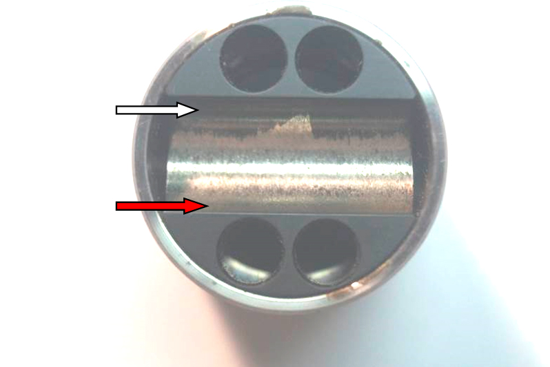 Фото 13. Износ металла (красная стрелка) и не повреждённое чёрное антиизносное (антифрикционное) покрытие (белая стрелка) на толкателе (стакане, поршне) плунжера в месте установки ролика