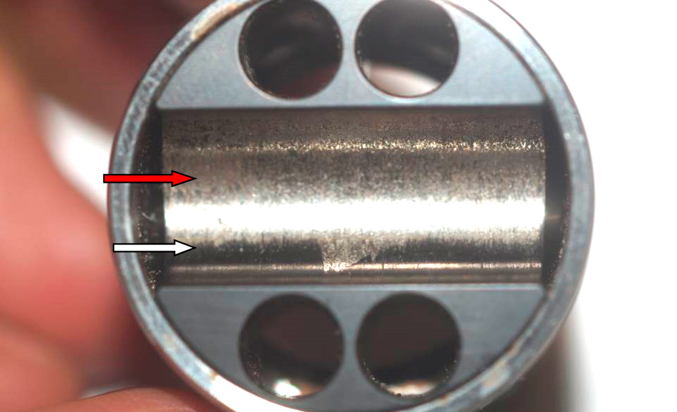 Фото 14. Износ металла (красная стрелка) и не повреждённое чёрное антиизносное (антифрикционное) покрытие (белая стрелка) на толкателе (стакане, поршне) плунжера в месте установки ролика