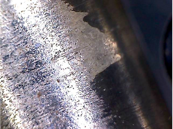 Фото 15. Износ металла и не повреждённое чёрное антиизносное (антифрикционное) покрытие в месте установки ролика. Вид через микроскоп – увеличение в 10 раз