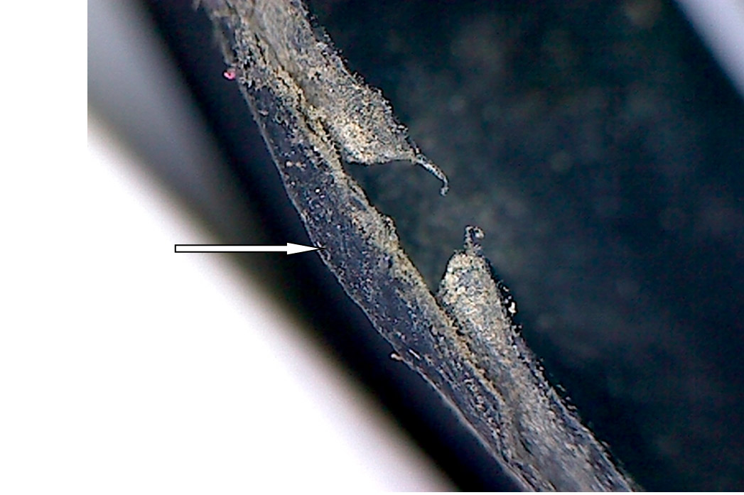 Фото 32. Вид торцевой части в районе трещины и сквозных отверстий. Отсутствие изменения структуры материала резины в виде выкрашивания и разрушения (показано белой стрелкой). Вид через микроскоп – увеличение в 20 раз.