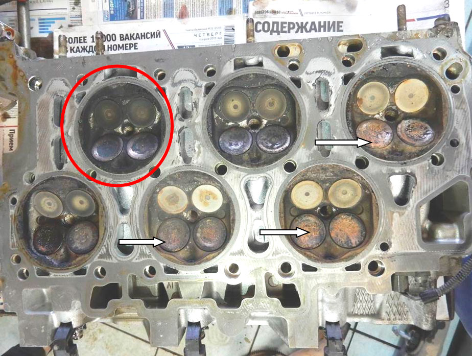 Фото 18. Камера сгорания 1-го цилиндра (показана в красном круге) имеет наиболее закопчённый внешний вид. На тарелках впускных клапанов зафиксированы коррозийные отложения (показаны белыми стрелками)